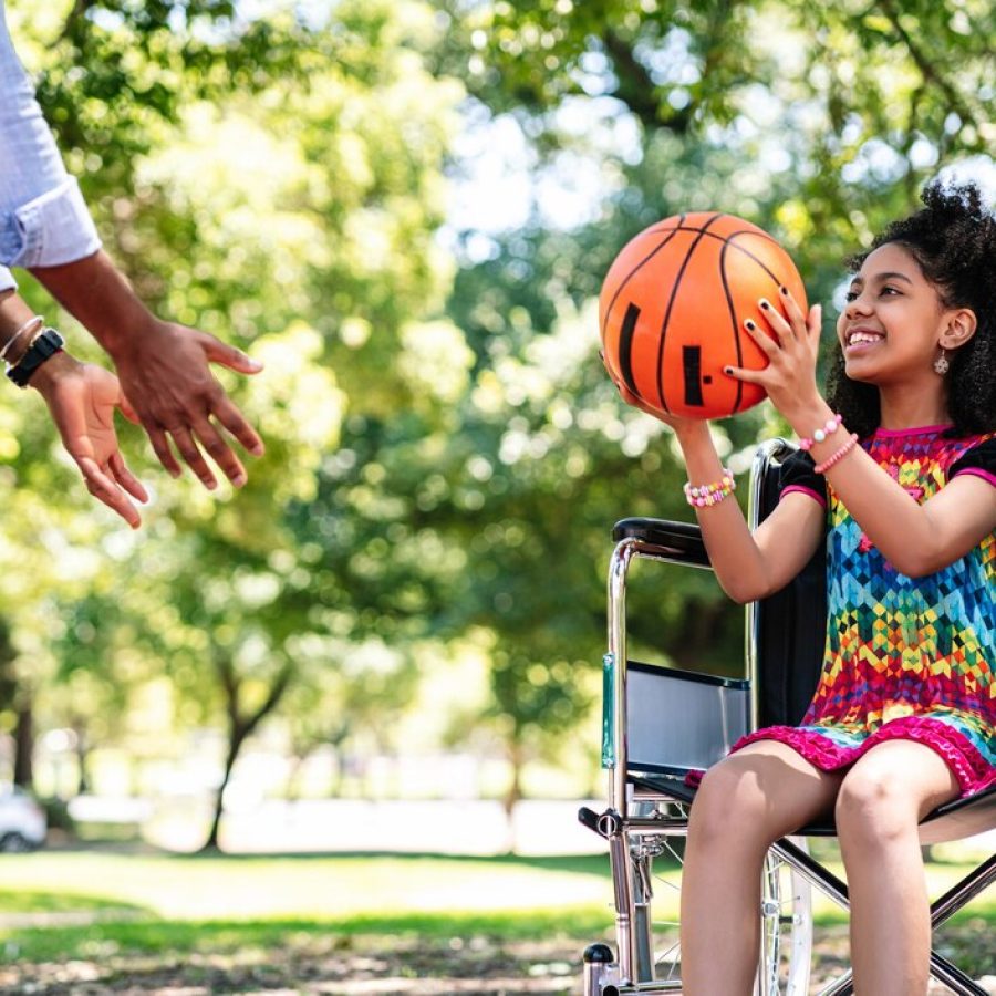 Little girl in wheelchair playing basketball with father